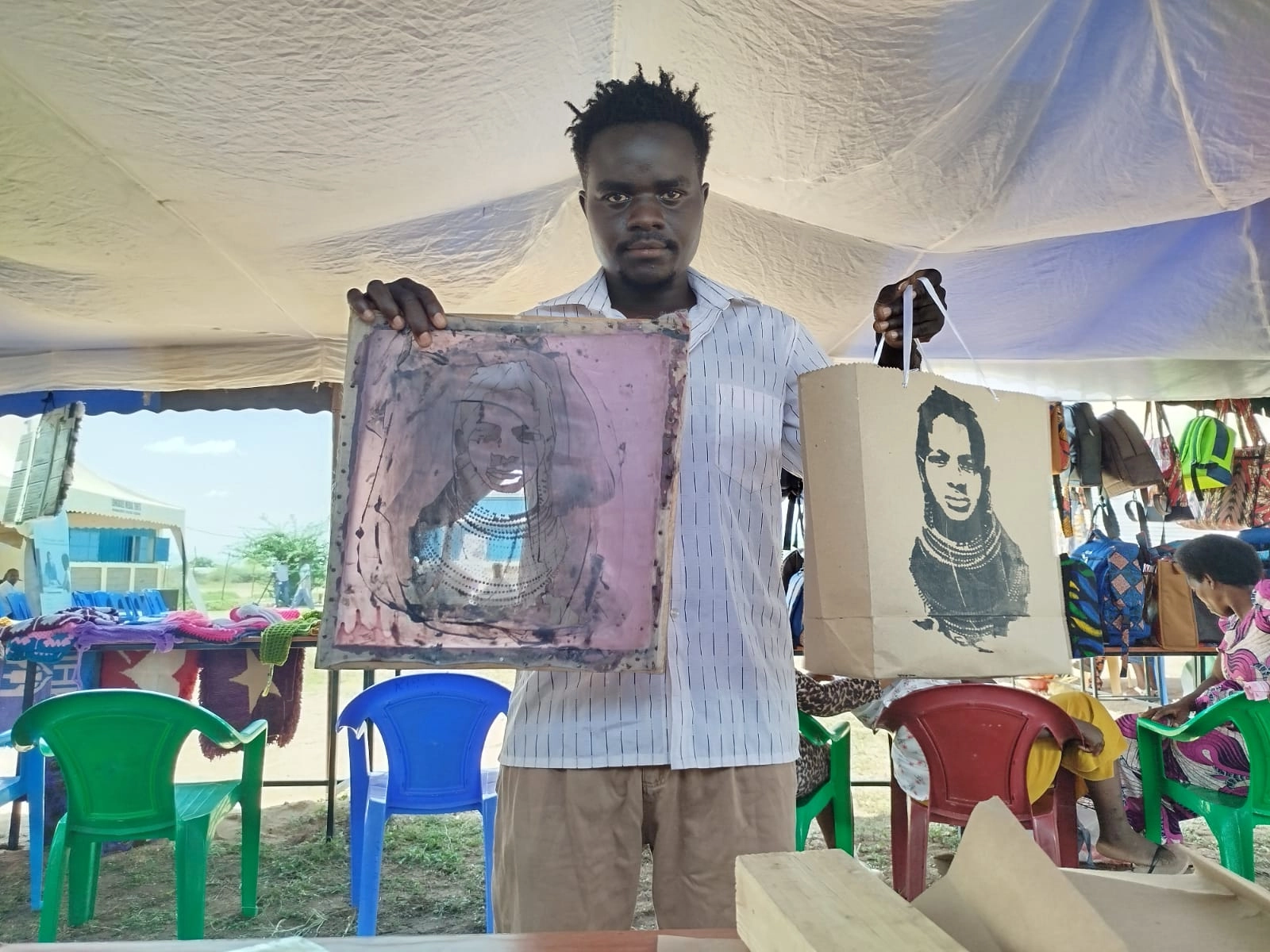 a young man carrying a finished khaki bag and the stencil used to decorate it