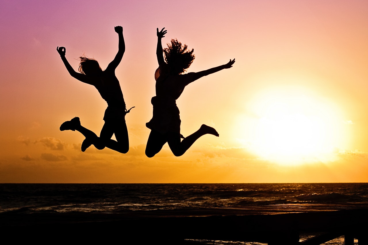 a silhouette of two young people jumping in jubilation mid-air